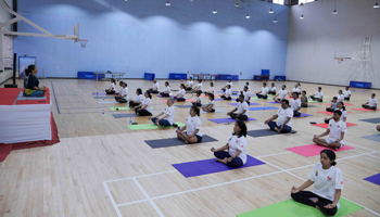 A photo from yoga workshop held on campus with a group of about 30 participants seated on their yoga mats in a spacious room in front of a yoga instructor