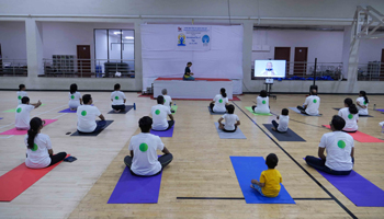 A photo from yoga workshop held on campus with a group of about 30 participants seated on their yoga mats in a spacious room in front of a yoga instructor