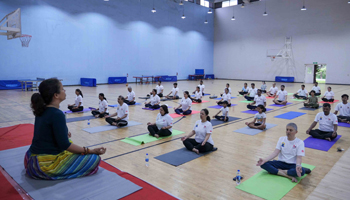 A photo from yoga workshop held on campus with a group of about 30 participants seated on their yoga mats in a spacious room in front of a yoga instructor