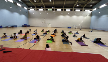 A photo from yoga workshop held on campus with a group of about 30 participants seated on their yoga mats in a spacious room in front of a yoga instructor